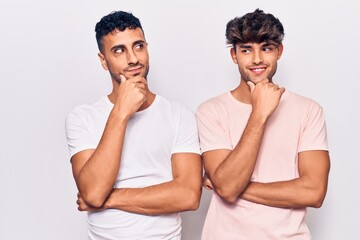 Young gay couple wearing casual clothes with hand on chin thinking about question, pensive expression. smiling with thoughtful face. doubt concept.