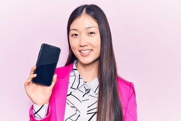 Young beautiful chinese woman holding smartphone showing screen looking positive and happy standing and smiling with a confident smile showing teeth
