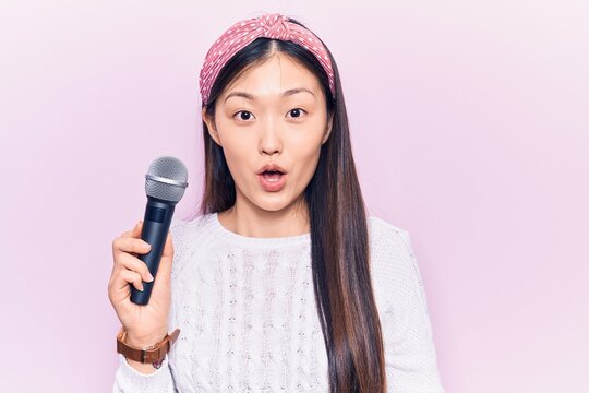 Young beautiful chinese woman singing song using microphone scared and amazed with open mouth for surprise, disbelief face