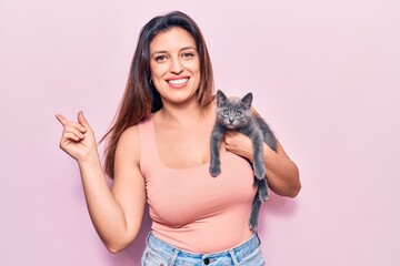 Young beautiful latin woman holding cat smiling happy pointing with hand and finger to the side
