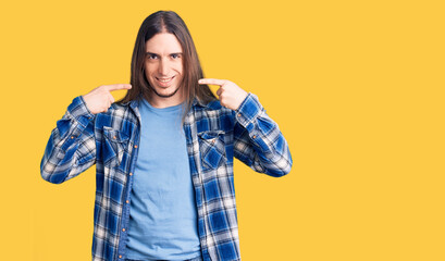 Young adult man with long hair wearing casual shirt smiling cheerful showing and pointing with fingers teeth and mouth. dental health concept.