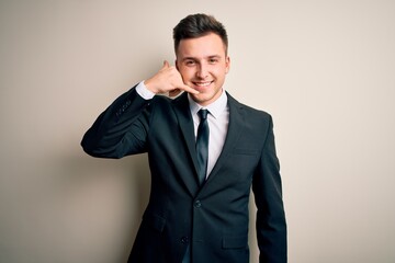 Young handsome business man wearing elegant suit and tie over isolated background smiling doing phone gesture with hand and fingers like talking on the telephone. Communicating concepts.