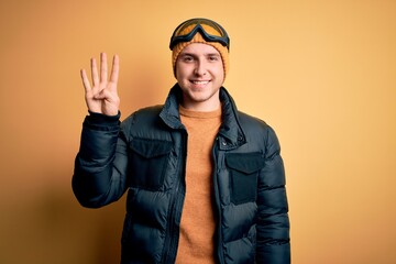Young handsome caucasian man wearing hat, coat and ski glasses for winter and snow weather showing and pointing up with fingers number four while smiling confident and happy.