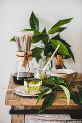 Coffee and dessert setup. Green matcha cheesecake and brewed pour-over coffee in glass flask on rustic wooden kitchen counter, white wall at background. Healthy, vegan, vegetarian, low calorie food