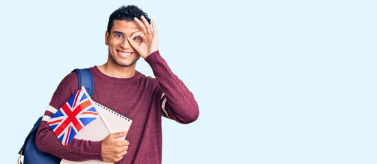 Fototapeta premium Hispanic handsome young man exchange student holding uk flag smiling happy doing ok sign with hand on eye looking through fingers