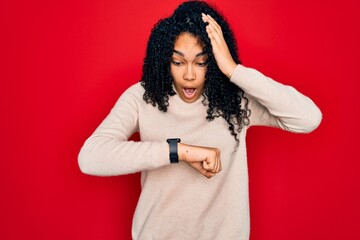 Young african american curly woman wearing casual turtleneck sweater over red background Looking at the watch time worried, afraid of getting late