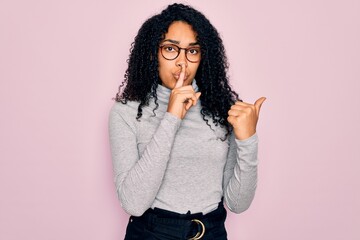 Young african american woman wearing turtleneck sweater and glasses over pink background asking to be quiet with finger on lips pointing with hand to the side. Silence and secret concept.