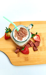 Chocolate milkshake with strawberries and pieces of chocolate on wooden table and white background