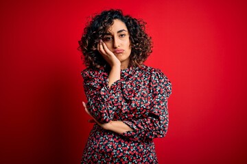 Young beautiful curly arab woman wearing casual floral dress standing over red background thinking looking tired and bored with depression problems with crossed arms.