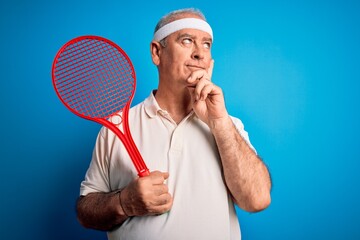Middle age hoary sportsman playing tennis using racket over isolated blue background serious face thinking about question, very confused idea
