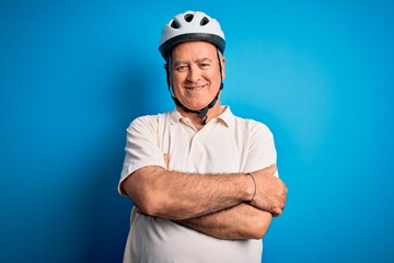 Middle age hoary cyclist man wearing bike security helmet over isolated blue background happy face smiling with crossed arms looking at the camera. Positive person.