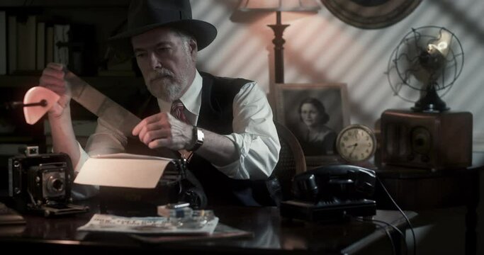 A dramatically lit scene of a private investigator from the 1940's era sitting in his office examining a roll of film negatives.
