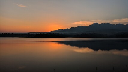 Landscape silhouette of mountains from the edge of the reservoir when the sun sets.