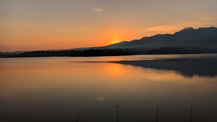 Fototapeta premium Landscape silhouette of mountains from the edge of the reservoir when the sun sets.