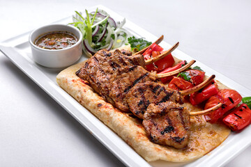Pork, lamb ribs on pita bread, with baked bell pepper and sauce, on a white plate