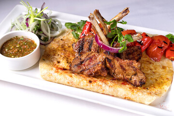 Pork, lamb ribs on pita bread, with baked bell pepper and sauce, on a white plate