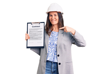 Young beautiful brunette woman wearing architect hardhat holding contract pointing finger to one self smiling happy and proud