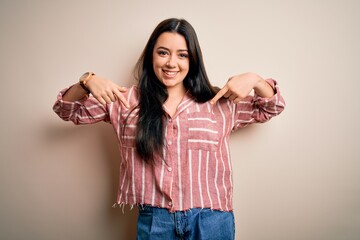 Young brunette woman wearing casual striped shirt over isolated background looking confident with smile on face, pointing oneself with fingers proud and happy.