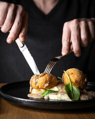 Person eating restaurant dish on black plate by fork and knife