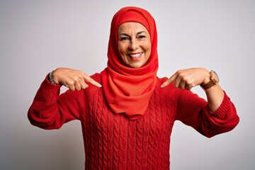 Middle age brunette woman wearing muslim traditional hijab over isolated white background looking confident with smile on face, pointing oneself with fingers proud and happy.
