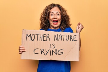 Fototapeta na wymiar Middle age woman asking for environment holding banner with mother nature is crying message screaming proud, celebrating victory and success very excited with raised arm