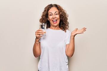 Middle age beautiful woman drinking glass of water to refreshment over white background celebrating achievement with happy smile and winner expression with raised hand