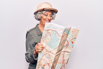 Senior grey-haired woman wearing explorer hat holding map looking positive and happy standing and smiling with a confident smile showing teeth