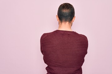 Young handsome man with blue eyes wearing casual sweater standing over pink background standing...