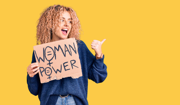 Young blonde woman with curly hair holding we need a change banner pointing thumb up to the side smiling happy with open mouth