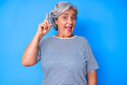 Senior hispanic grey- haired woman wearing casual clothes pointing finger up with successful idea. exited and happy. number one.