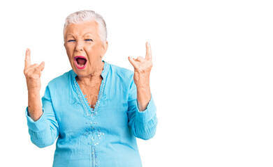 Senior beautiful woman with blue eyes and grey hair wearing summer dress shouting with crazy expression doing rock symbol with hands up. music star. heavy concept.