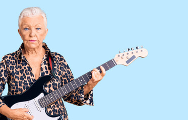 Senior beautiful woman with blue eyes and grey hair with modern look playing electric guitar thinking attitude and sober expression looking self confident