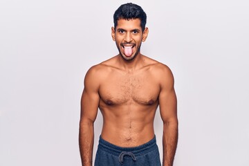 Young latin man standing shirtless sticking tongue out happy with funny expression. emotion concept.