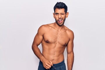 Young latin man standing shirtless winking looking at the camera with sexy expression, cheerful and happy face.