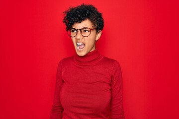 Fototapeta na wymiar Young beautiful african american afro woman wearing turtleneck sweater and glasses angry and mad screaming frustrated and furious, shouting with anger. Rage and aggressive concept.