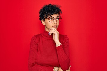 Fototapeta na wymiar Young beautiful african american afro woman wearing turtleneck sweater and glasses with hand on chin thinking about question, pensive expression. Smiling with thoughtful face. Doubt concept.