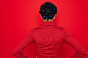 Fototapeta na wymiar Young beautiful african american afro woman wearing turtleneck sweater and glasses standing backwards looking away with arms on body