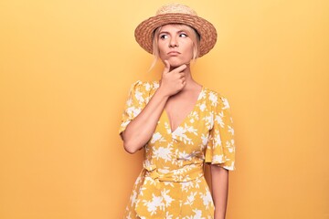 Beautiful blonde woman on vacation wearing summer hat and dress over yellow background Touching painful neck, sore throat for flu, clod and infection