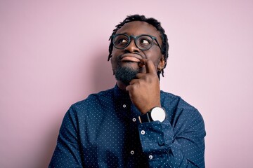 Young handsome african american man wearing casual shirt and glasses over pink background with hand on chin thinking about question, pensive expression. Smiling with thoughtful face. Doubt concept.