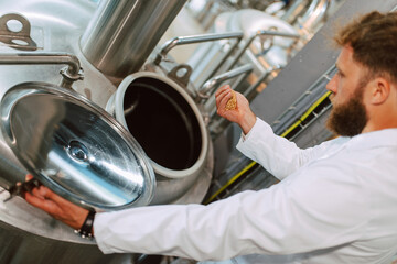 Technologist specialist in white protective suit working in beverage factory and holds hops in the palm of his hand while brewing