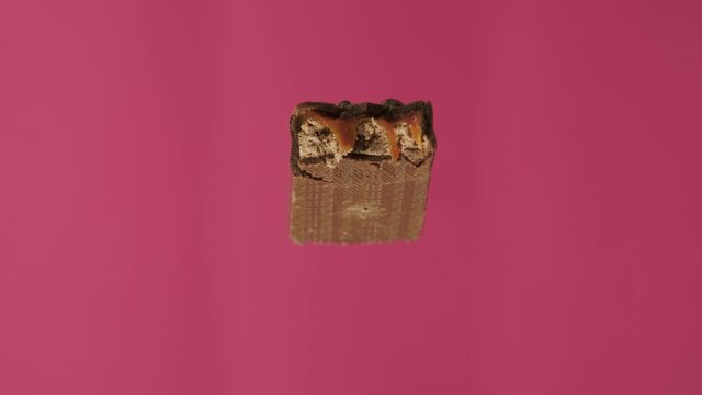 A delicious and unhealthy chocolate bar rotates on a pink background. Bitten sweets isolated. The unpacked bar is spinning. Nougat and caramel inside candy bar chocolate