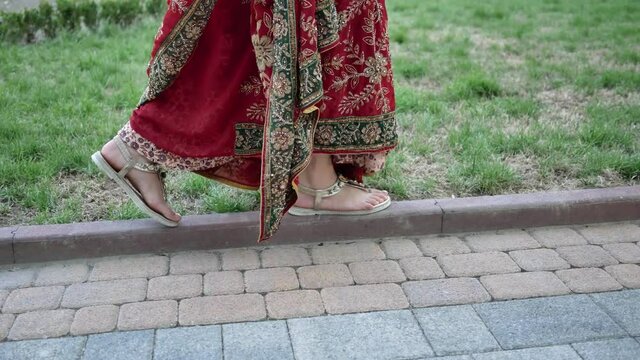 Closeup of Indian woman feet in sandals walking in park streets of city of India dressed in red Sari, decorated with traditional ornaments