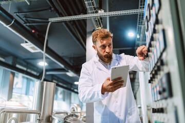  Professional caucasian handsome technologist expert in white uniform standing in pharmaceutical or food factory  - production plant checking productivity and quality using tablet computer.