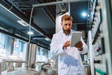  Professional caucasian handsome technologist expert in white uniform standing in pharmaceutical or food factory  - production plant checking productivity and quality using tablet computer.