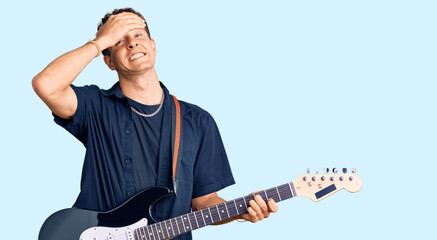 Young handsome man playing electric guitar stressed and frustrated with hand on head, surprised and angry face