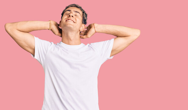 Young handsome man wearing casual white tshirt relaxing and stretching, arms and hands behind head and neck smiling happy