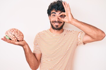 Handsome young man with curly hair and bear holding brain as mental health concept smiling happy...
