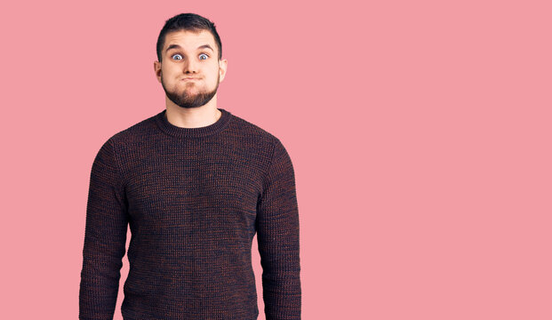 Young handsome man wearing casual sweater puffing cheeks with funny face. mouth inflated with air, crazy expression.