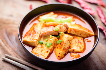 Kimchi soup with tofu and pork in a bowl and chopsticks on wooden background, Korean food (Kimchi Jjigae)