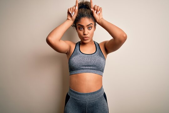 Young african american sportswoman doing sport wearing sportswear over white background doing funny gesture with finger over head as bull horns